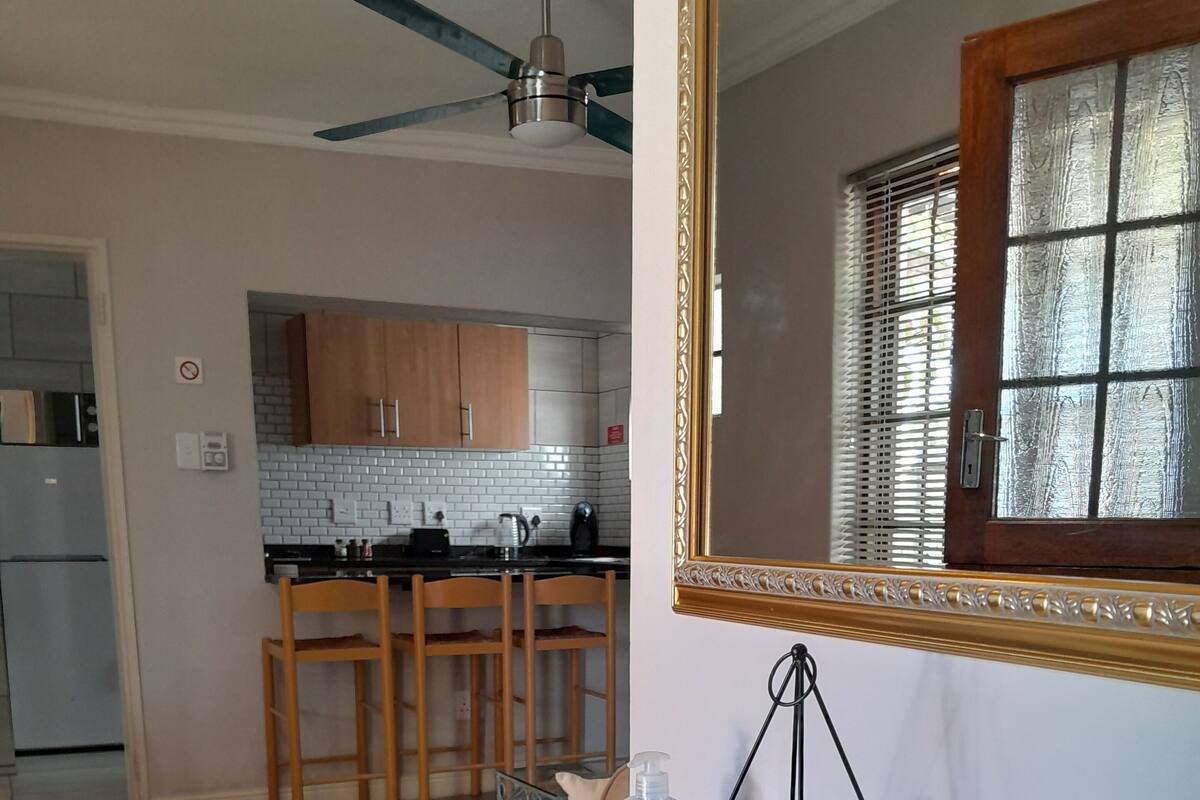 A dining area with a round glass table, a mirror with a decorative frame, and a potted plant.