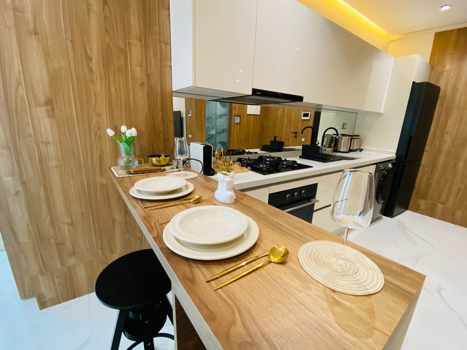 Une cuisine moderne avec un plan de travail en bois, des appareils électroménagers blancs et une cuisinière noire.