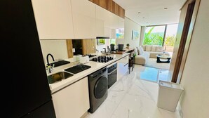 A modern kitchen with a dishwasher, stove, and sink. There is a dining area with a sofa and a coffee table. - Stay'Inn - Anfa Flores (Casablanca)