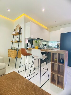 A modern kitchen with white cabinets, a wooden bar counter, and a built-in stove. - Stay'Inn - Anfa Flores (Casablanca)