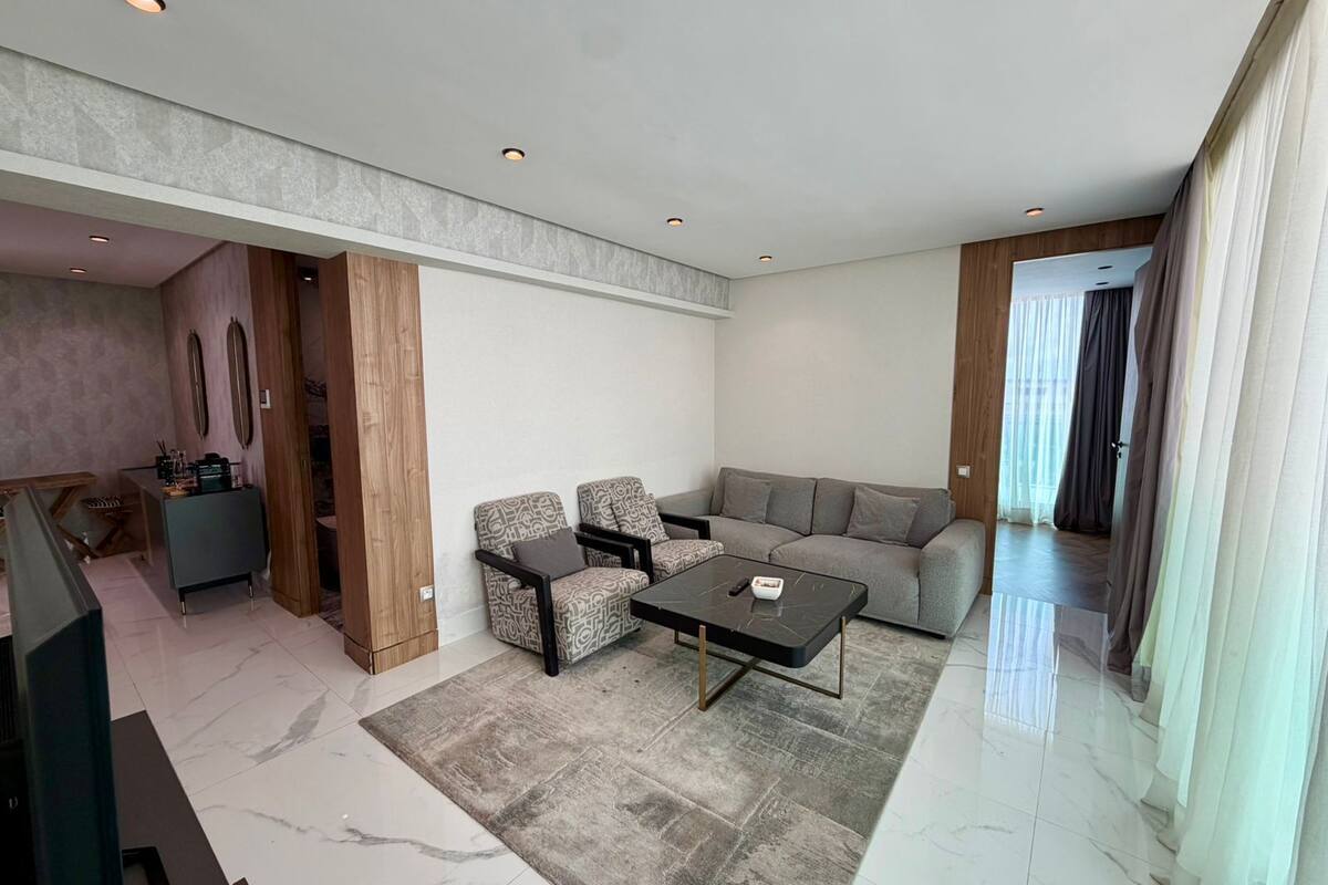 A modern living room with a sofa, two armchairs, a coffee table, and a TV.