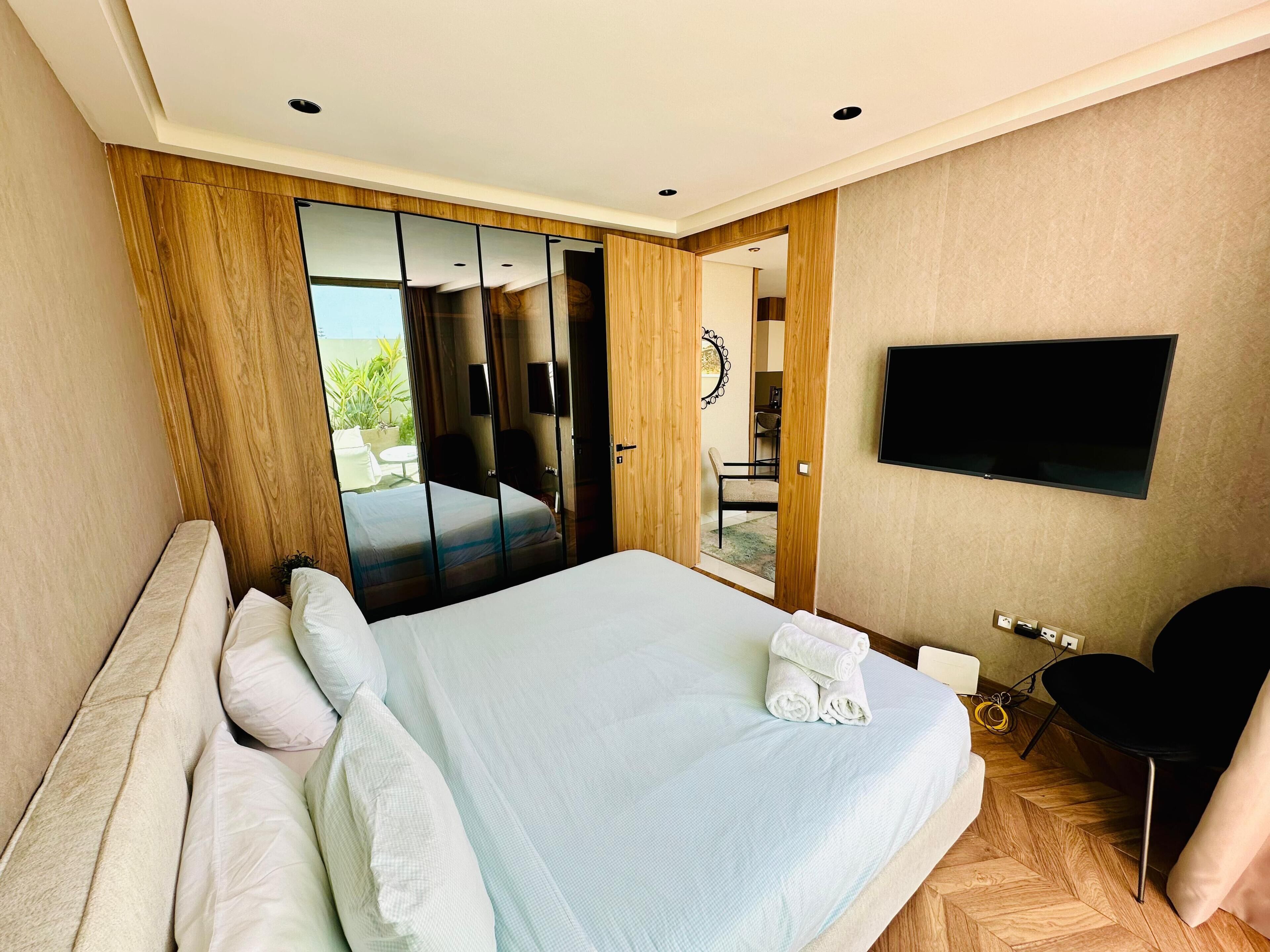 Une chambre d’hôtel avec un grand lit, un téléviseur fixé au mur et une porte coulissante donnant sur un balcon.