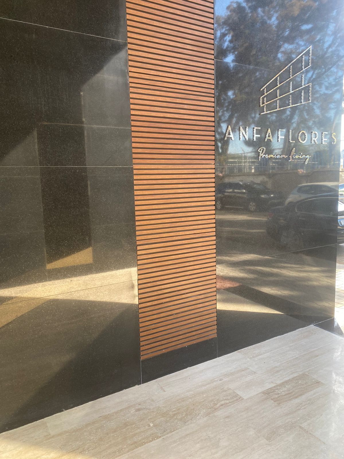 Une façade moderne, avec un panneau vertical en bois et une fenêtre en verre sur laquelle est inscrit le nom « ANFAFLORES Premium Living ».