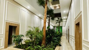 A hallway with a central planter featuring palm trees and various plants, flanked by doors and a polished marble floor. - Stay'Inn - Anfa Flores (Casablanca)