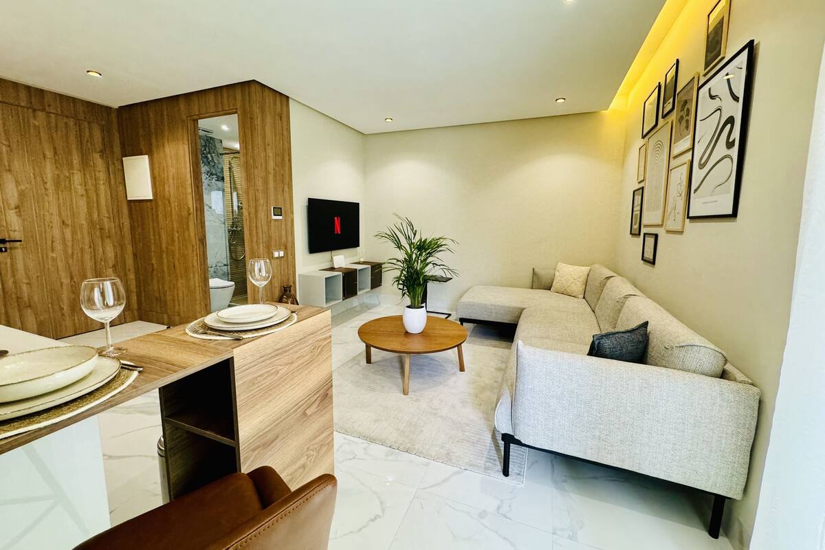 A modern living room with a sofa, coffee table, and dining area with a TV.