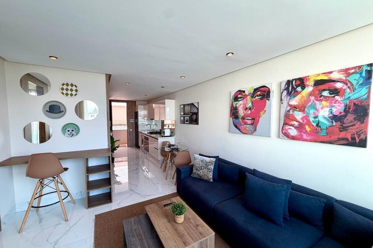 A modern living room with a blue sofa, a coffee table, and a dining area in the background.