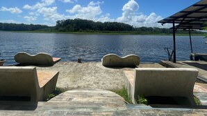 Vista de un lago con una terraza de concreto, sillas de descanso y un área techada.