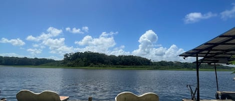 A lakeside view with a concrete deck, lounge chairs, and a covered area.