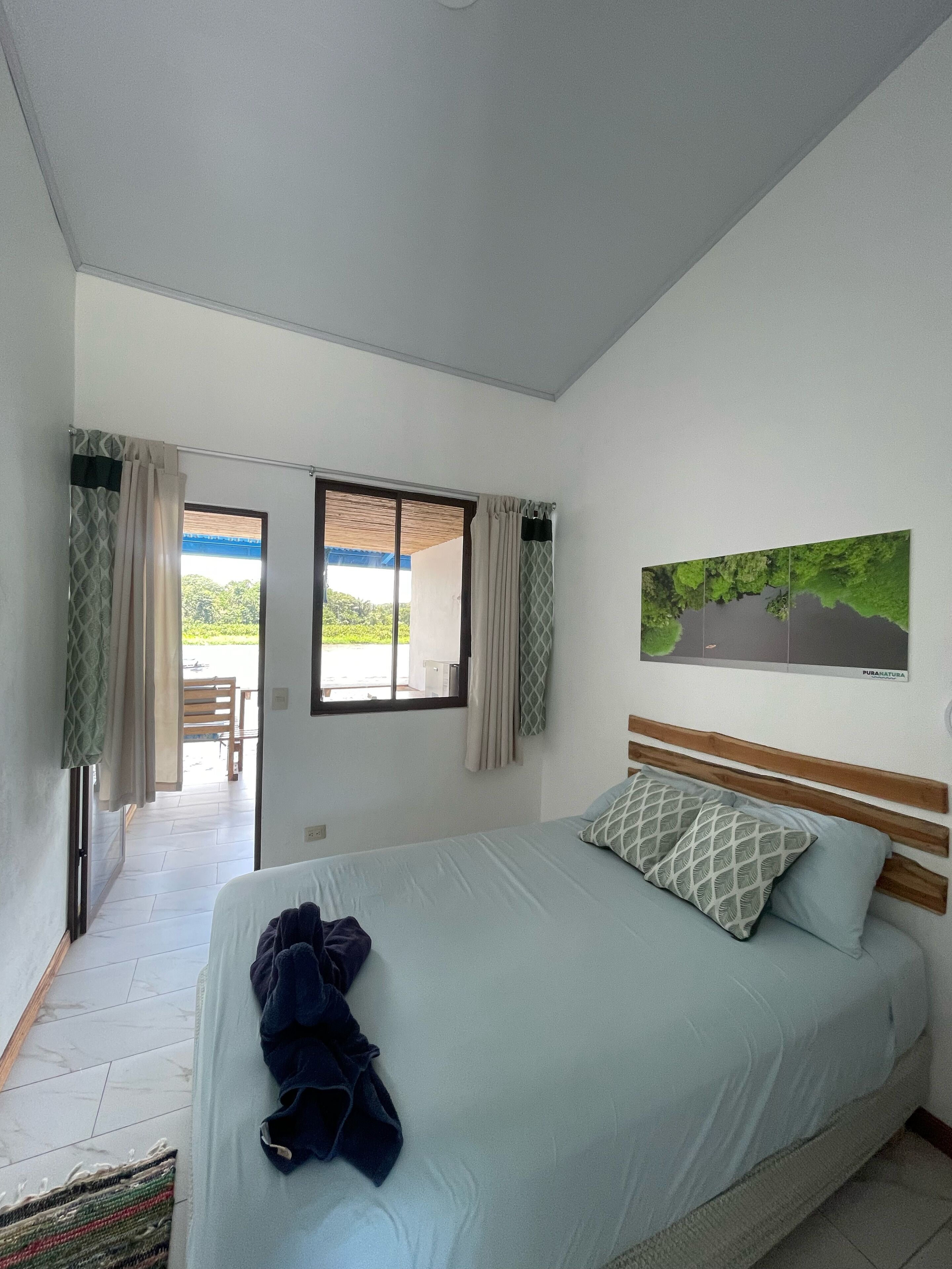 Un dormitorio con una cama, vistas al exterior y un cuadro en la pared.