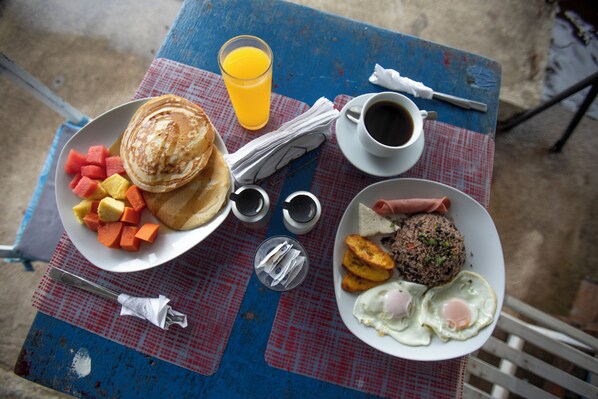A breakfast table with pancakes, fruit, eggs, and a cup of coffee.