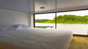 Un dormitorio con una cama grande, vistas a un lago y una banca frente a la ventana.