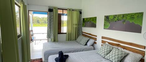 A hotel room with two beds, a view of greenery outside, and a large window with curtains.