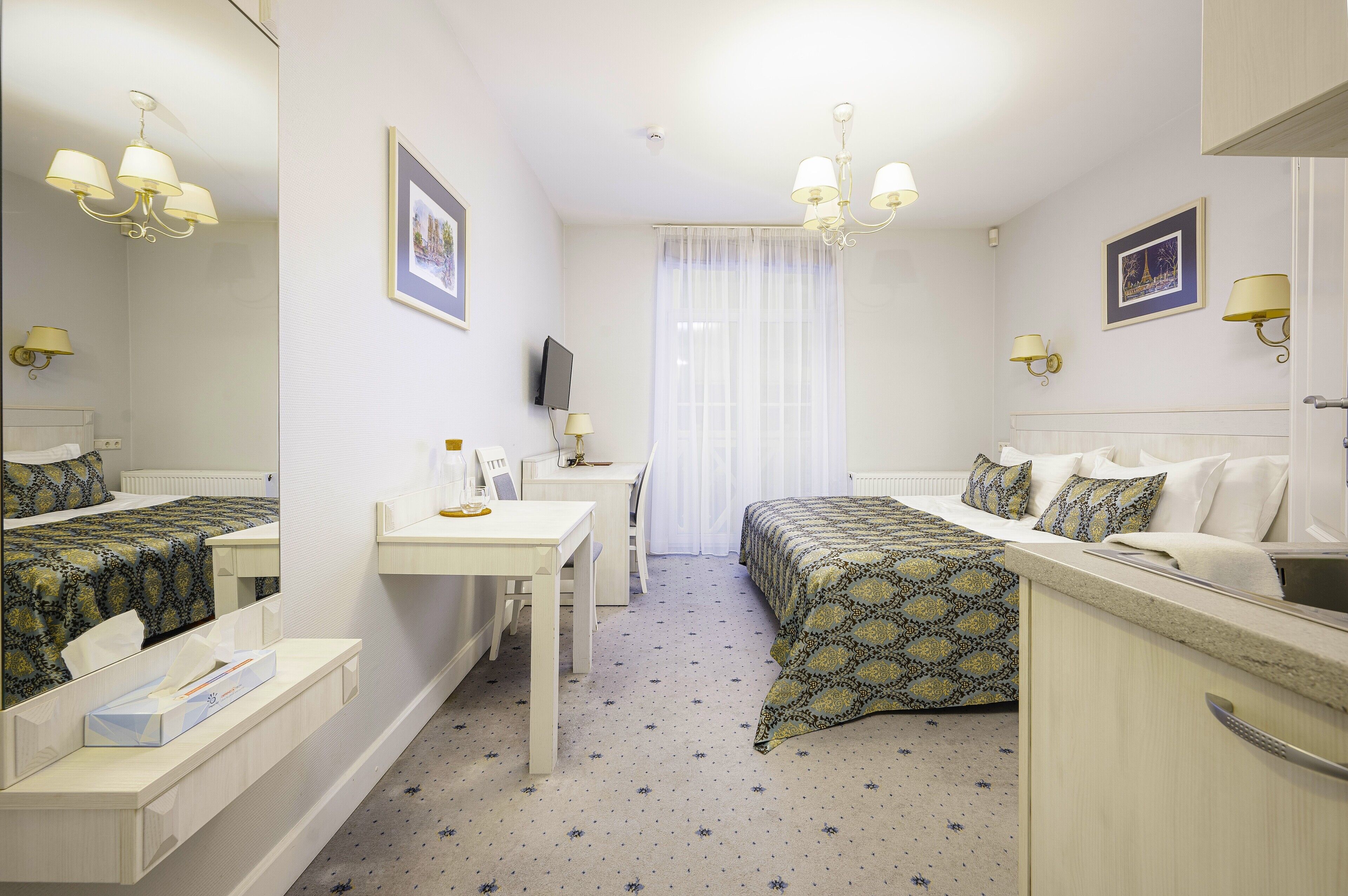 Habitación de hotel con cama, escritorio, silla, televisión y ventana con cortinas.