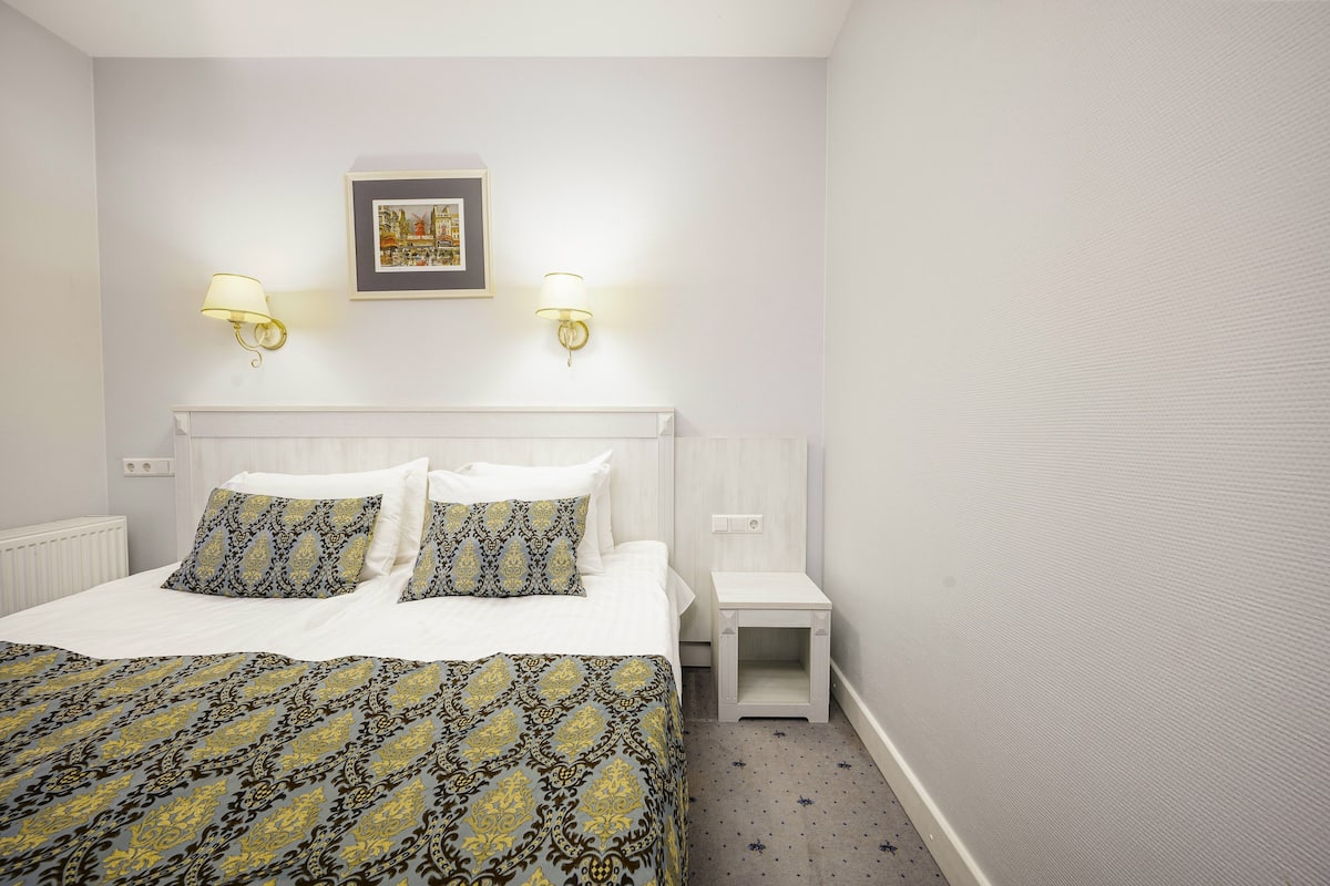 A neatly arranged hotel room with a bed, bedside tables, and wall-mounted lamps.