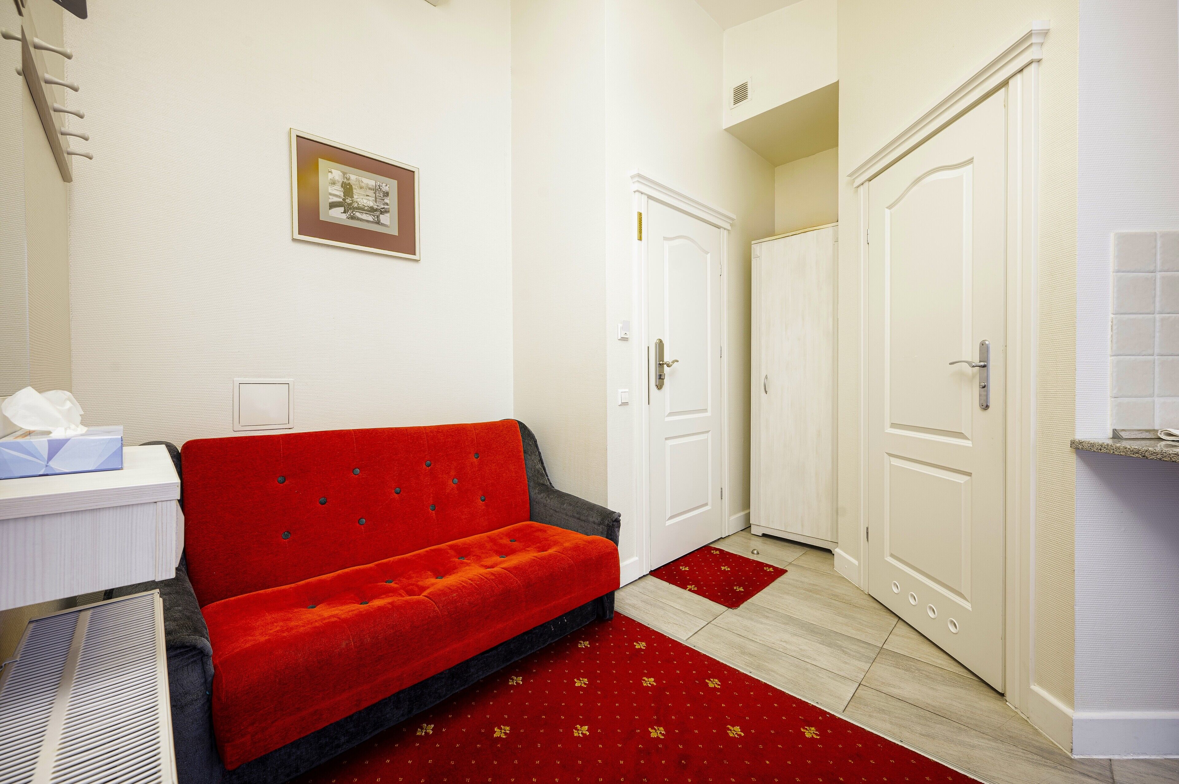Habitación de hotel con sofá rojo, puertas blancas y una mesita con una caja de pañuelos.