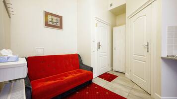 Habitación de hotel con sofá rojo, puertas blancas y una mesita con una caja de pañuelos.