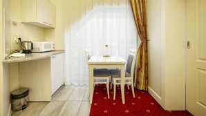 Cocina compacta con microondas, un pequeño cubo de basura y una ventana con cortinas traslúcidas.