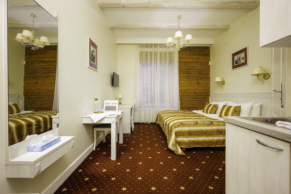 A hotel room with a bed, a desk, a chair, a mirror, a television, and a window with curtains.