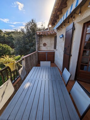 A wooden deck with a table and chairs, a barbecue area, and a view of the surrounding greenery.