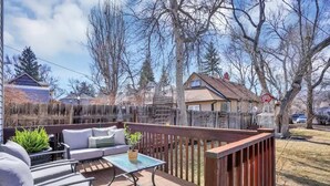 An outdoor deck with a sofa and table, surrounded by a wooden fence and trees. - A+ Location Cozy Renovated Home! (Colorado Springs)