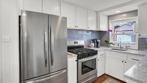 A modern kitchen with white cabinets, stainless steel appliances, a gas stove, and a window with a view. - A+ Location Cozy Renovated Home! (Colorado Springs)