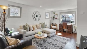 A modern living room with a sofa, coffee table, and a desk area with a chair. - A+ Location Cozy Renovated Home! (Colorado Springs)
