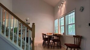 A dining area with a table and chairs, a staircase with white railings, and a window with curtains.