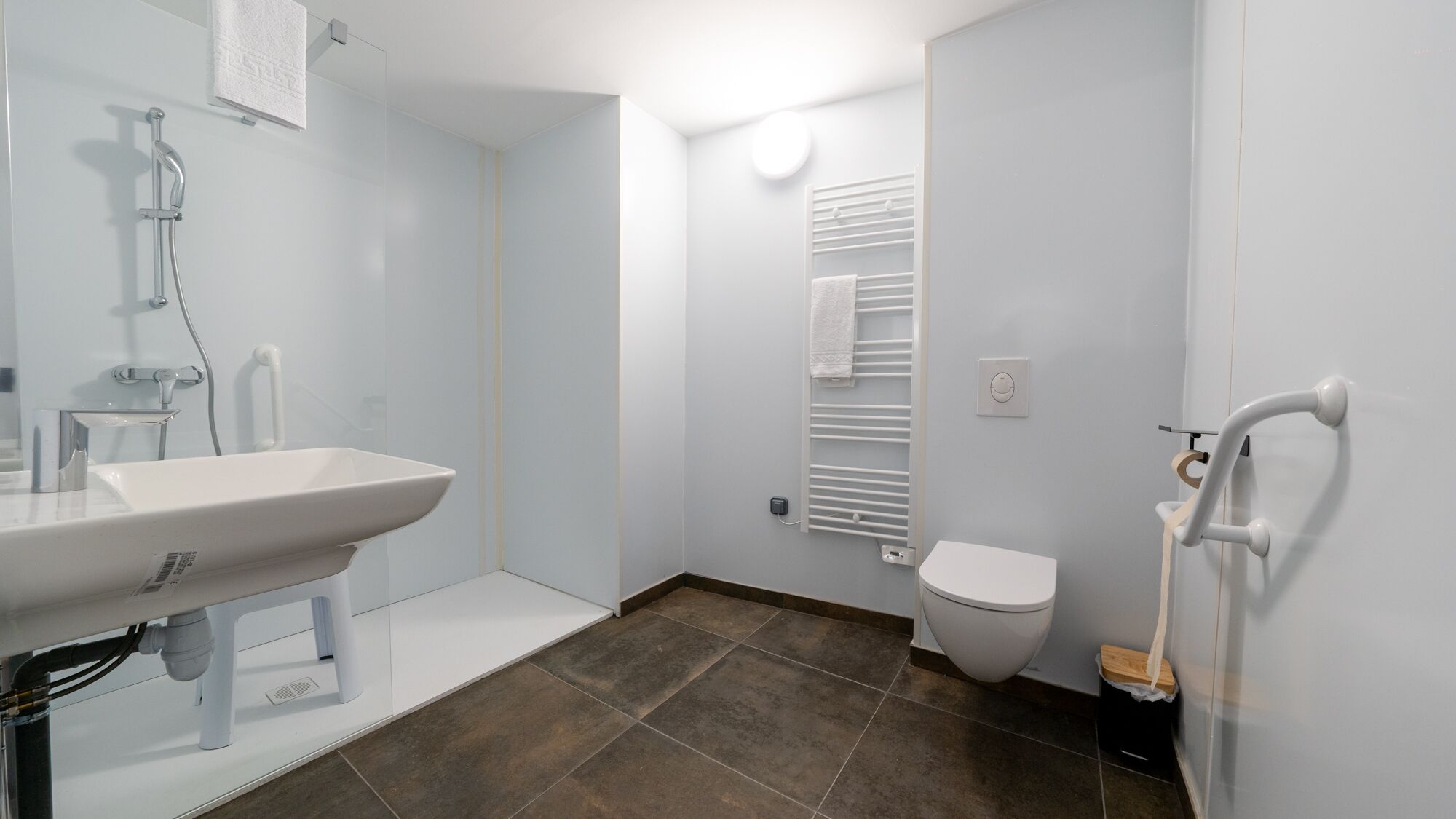A modern bathroom with a white sink, a shower, a toilet, and a towel rack.