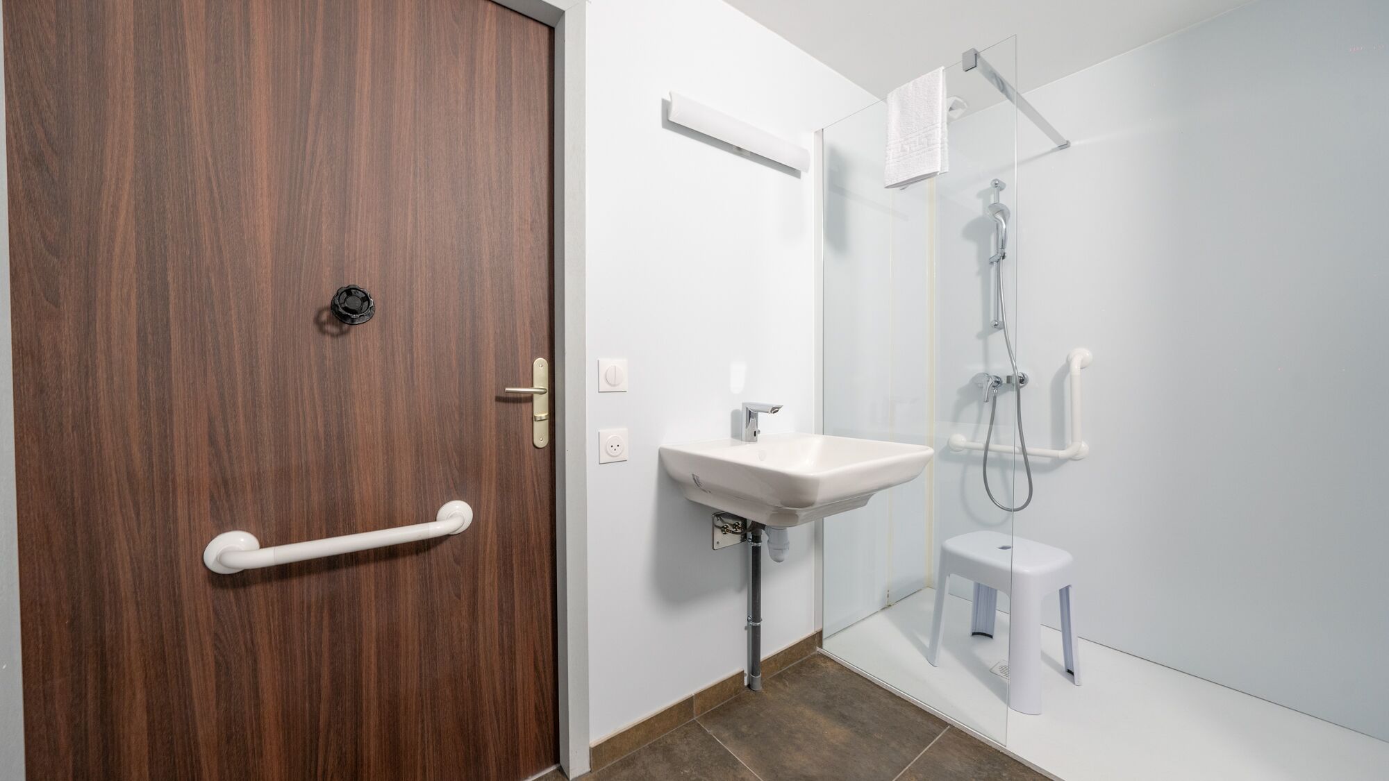 Une salle de bain moderne avec une porte en bois, un lavabo blanc, une cabine de douche en verre et des toilettes blanches.