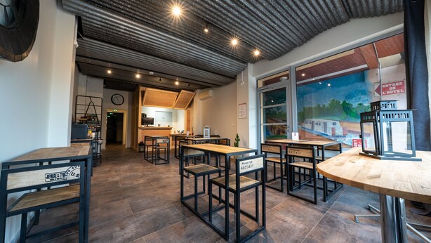 A modern cafe with wooden tables and chairs, a kitchen area, and a mural on the wall. - Hôtel des Docks (Digoin)