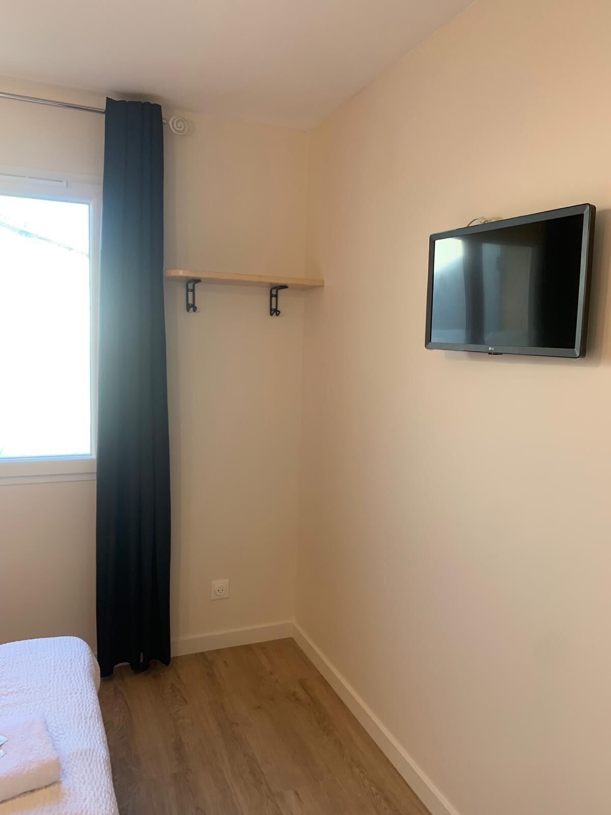 Um quarto com cama, TV fixada na parede e janela com cortinas.