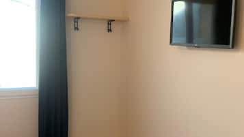Um quarto com cama, TV fixada na parede e janela com cortinas.