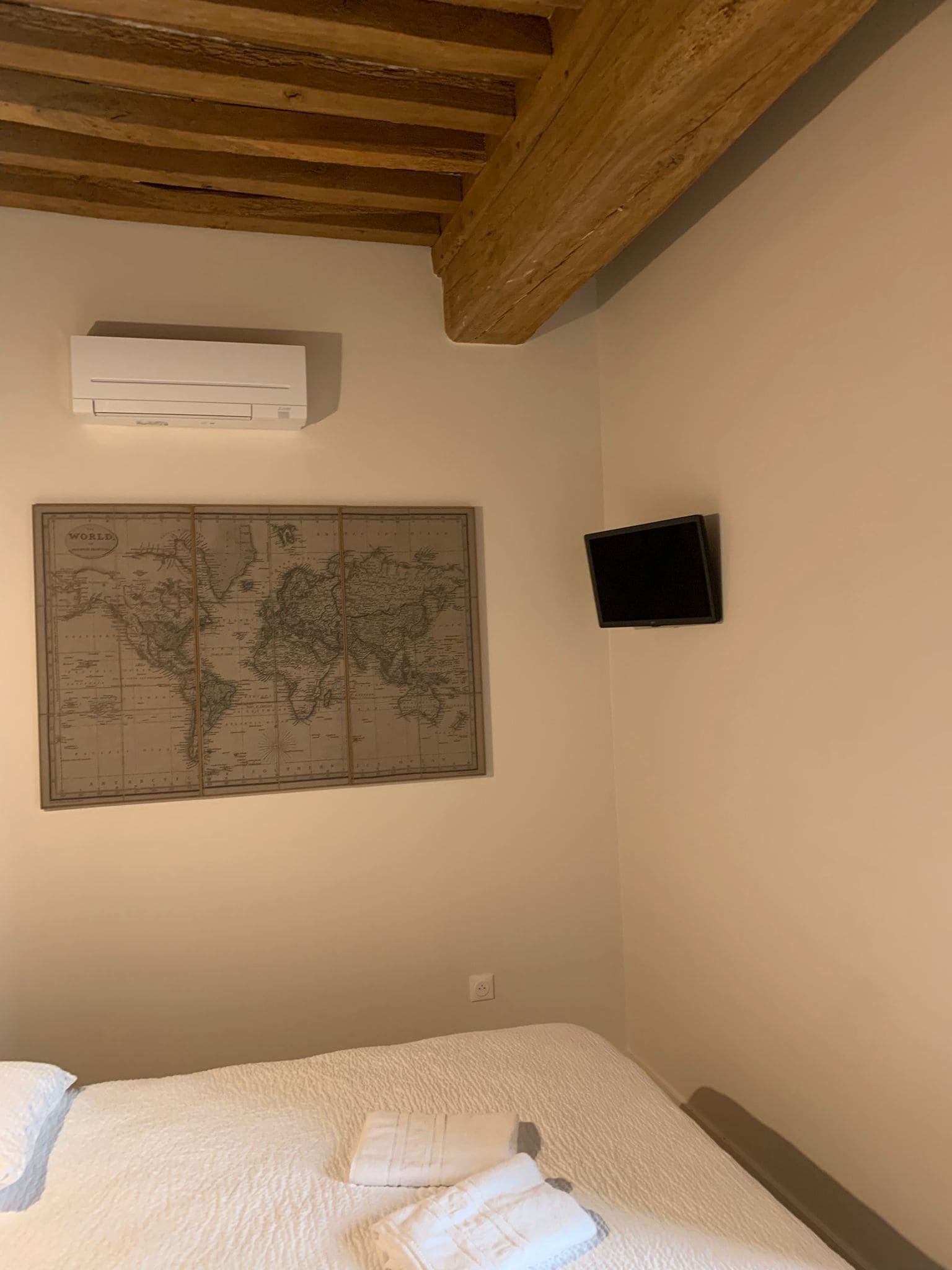 A bedroom with a bed, a world map, an air conditioner, and a flat-screen TV.