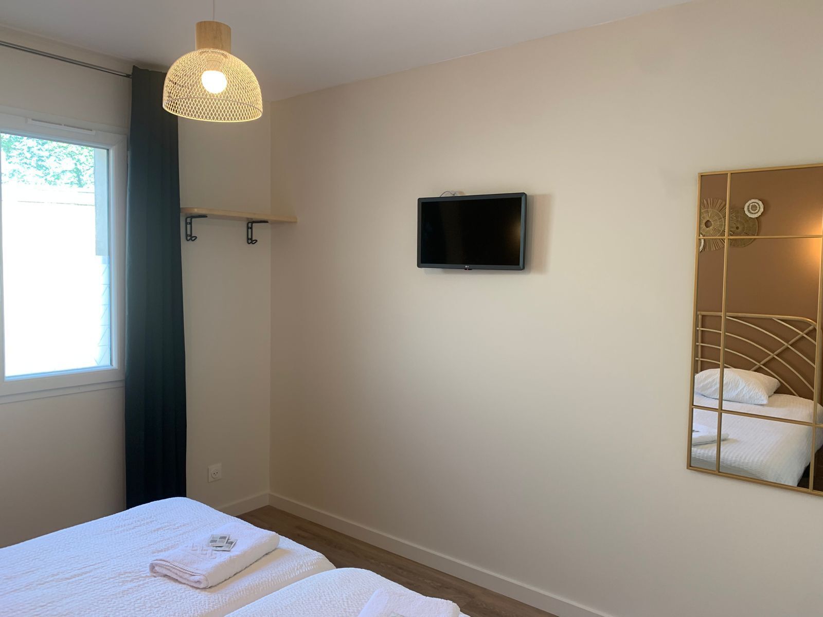 A bedroom with a bed, a television, a mirror, and a hanging light fixture.