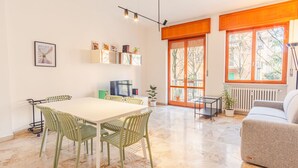 A dining area with a table and chairs, a television, and a bookshelf with books and decorative items. - Residenza Ponte Pietra (Verona)