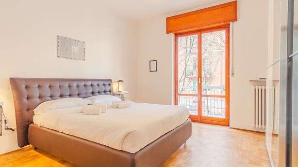 A bedroom with a large bed, a window with a view of trees, and a radiator. - Residenza Ponte Pietra (Verona)