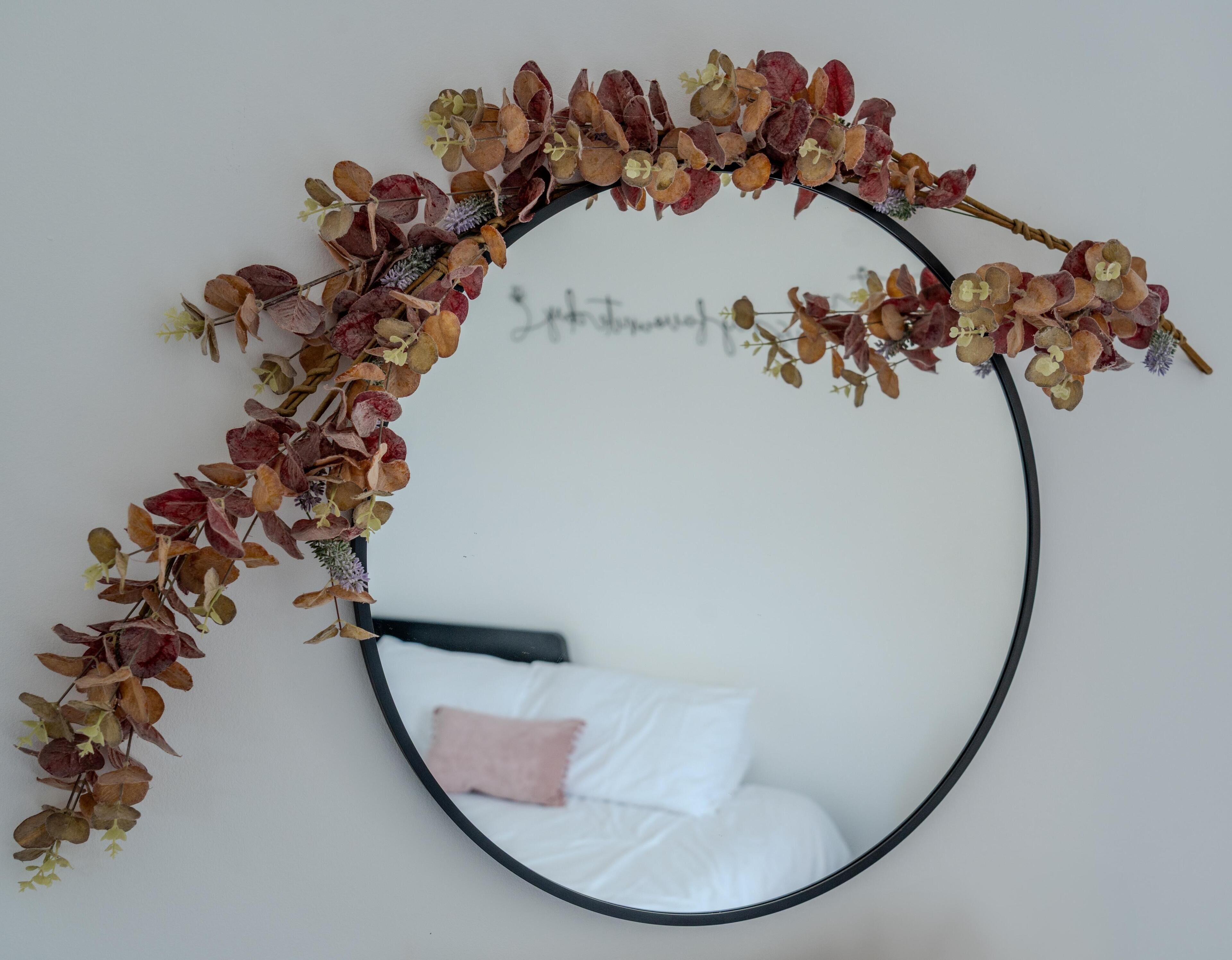 A circular mirror with a decorative arrangement of dried leaves and flowers.