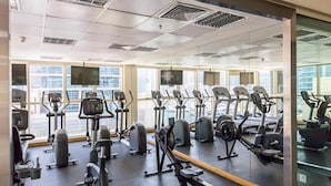 Ein Fitnessstudio mit verschiedenen Trainingsgeräten, großen Fenstern und einer Spiegelwand.
