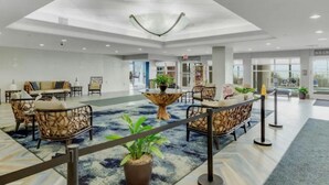 Een ruime lobby met een hoge plafond, zithoeken en een centrale plant.