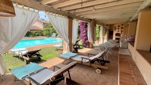 Ein überdachter Außenbereich mit Lounge-Möbeln und einem Pool im Hintergrund.