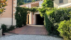 Eine Villa mit befestigter Auffahrt, die zu einem überdachten Eingang führt, umgeben von üppiger Vegetation und Bergen im Hintergrund.