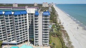 A high-rise hotel with multiple balconies, a swimming pool area, and a beachfront view. - Carolina Winds 1005-1BR OF Condo in Myrtle Beach (Myrtle Beach)