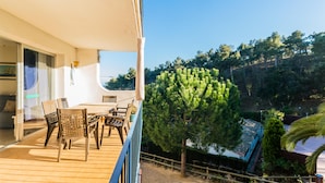 A balcony with a wooden table and chairs, a potted plant, and a view of a forested hillside. - AE-1 Charming Apartment in El Golfet (Calella de Palafrugell)