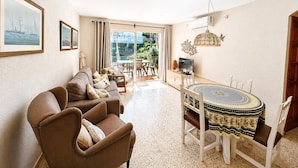 A living room with a sofa, a dining table with chairs, a TV, and a balcony with a view. - AE-1 Charming Apartment in El Golfet (Calella de Palafrugell)