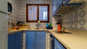 A kitchen with patterned tiles, a window with lace curtains, and blue cabinets. - AE-1 Charming Apartment in El Golfet (Calella de Palafrugell)