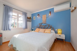 A bedroom with a bed, a nightstand, a wall-mounted air conditioner, and a window with curtains.