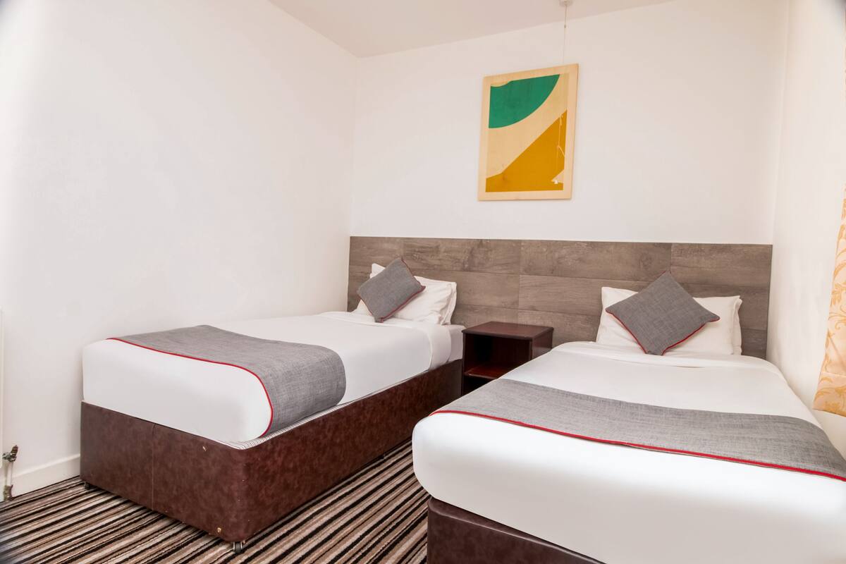 Une chambre d'hôtel avec deux lits, une tête de lit en bois, une moquette à rayures et un tableau abstrait accroché au mur.