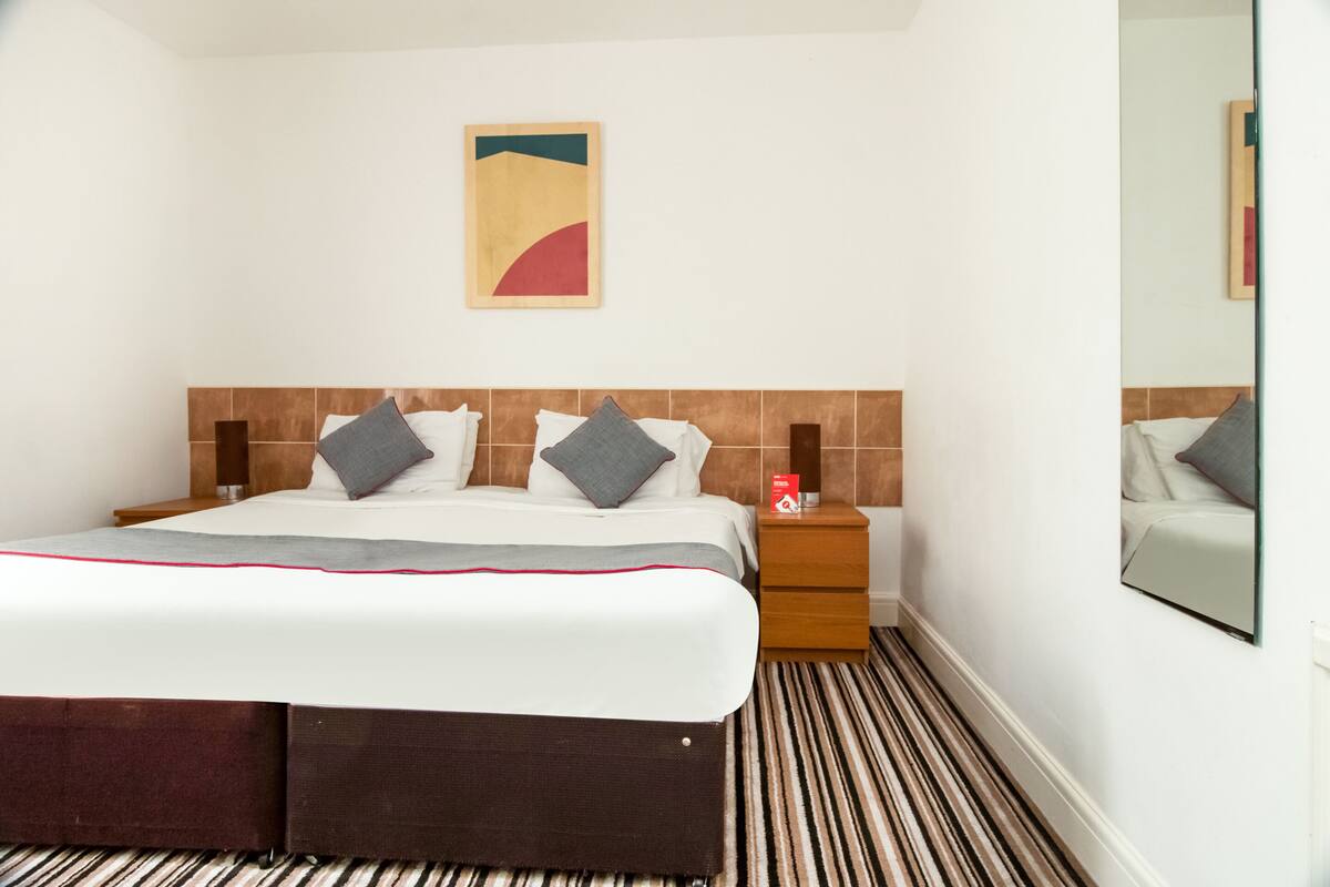 Une chambre d’hôtel comprenant un lit, une table de chevet, un miroir et une œuvre d’art murale.