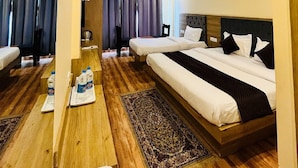 A hotel room with two beds, a wooden floor, a large rug, and a ceiling fan. - The Fragrance Hotel (Reasi)