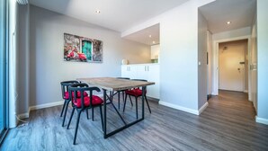 Un coin repas avec une table en bois et quatre chaises, une cuisine à l’arrière-plan et un couloir menant à une porte.